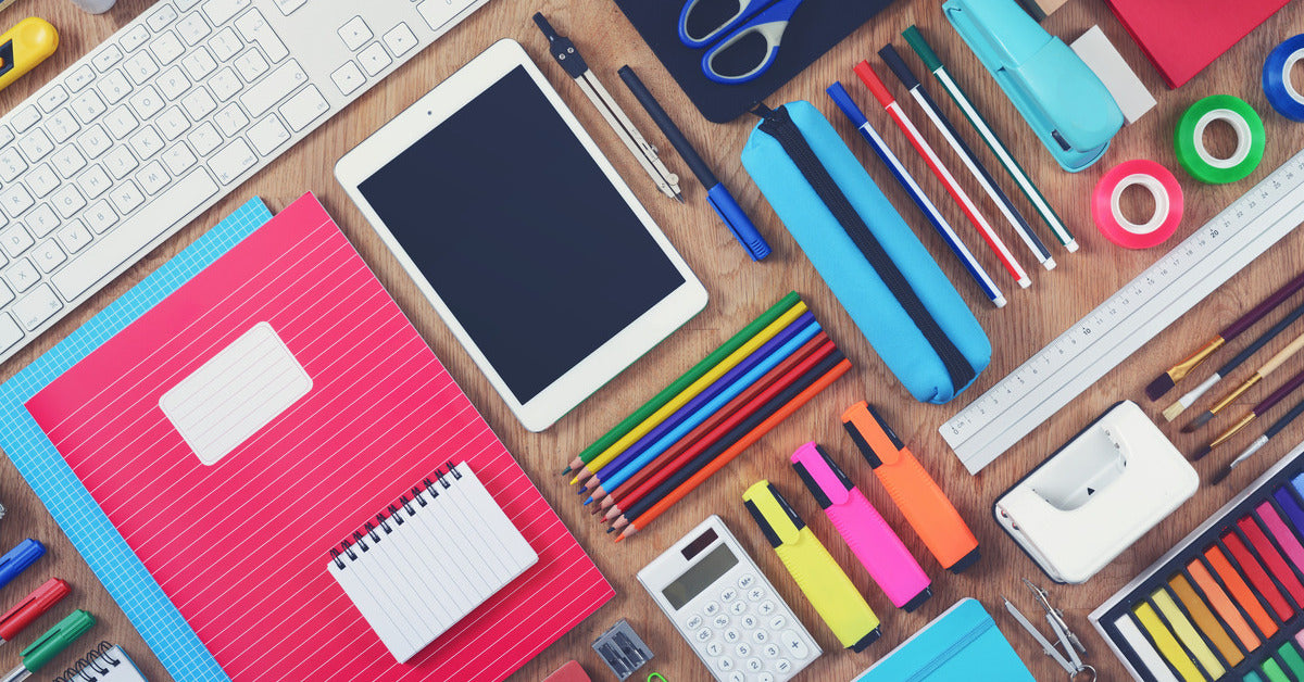 An array of colorful school supplies, including colored pencils, notebooks, and highlighters, neatly placed on a wooden table.