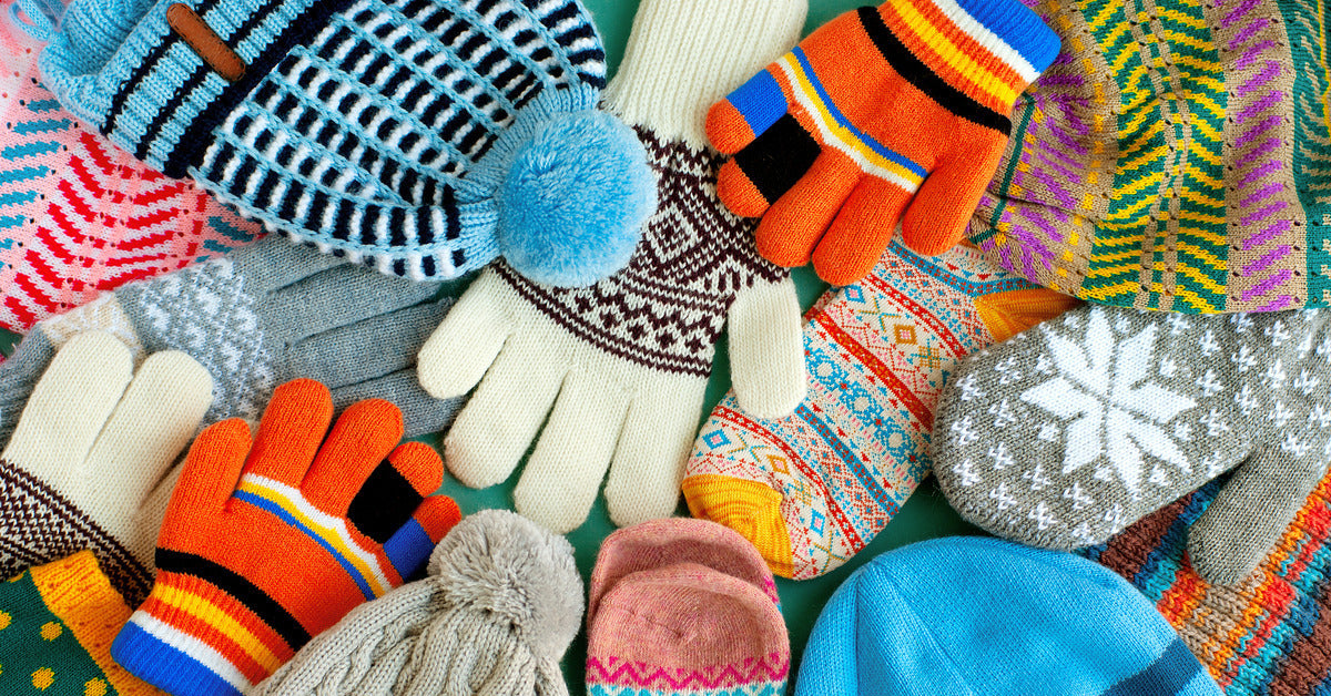 An array of colorful and patterned gloves, hats, mittens, and scarves lay on a table. There is an assortment of sizes.